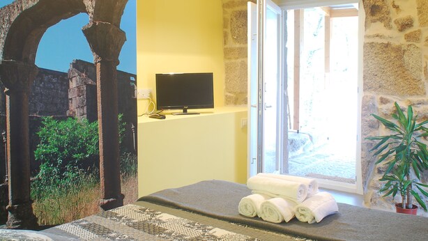 A room with stone arches, a television, a window with a view, and a potted plant. - Casa do Mosteiro (Xinzo de Limia)