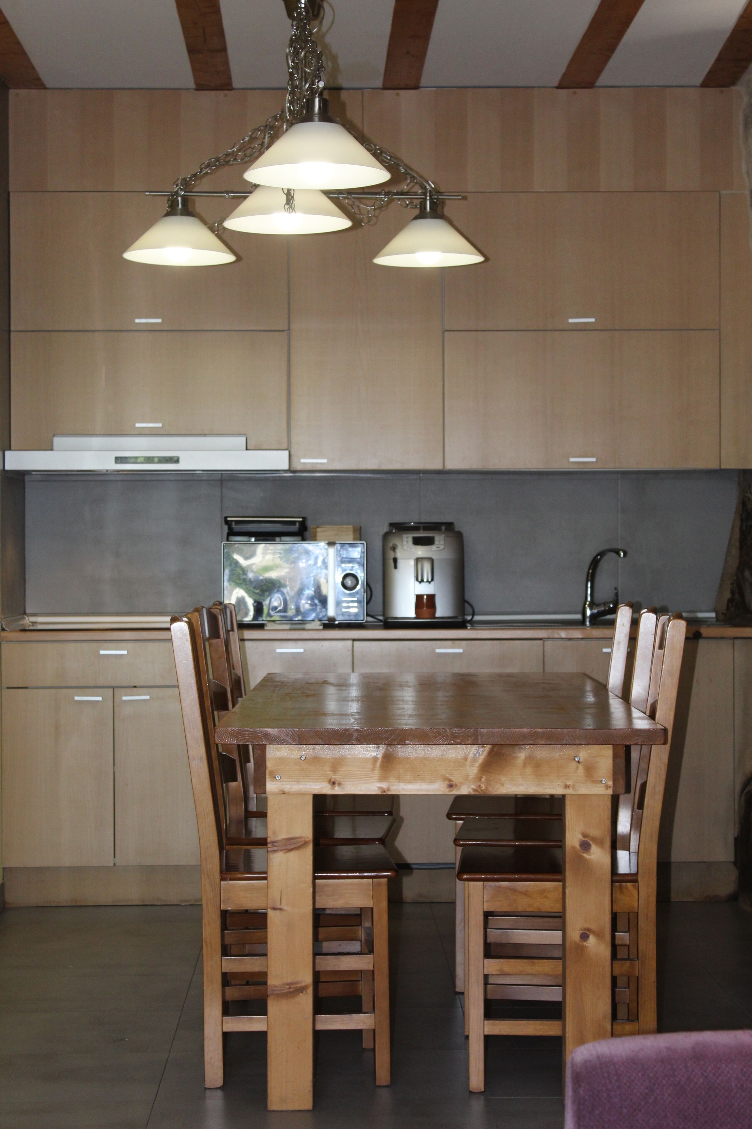 A modern kitchen with wooden cabinets, a stainless steel toaster, a coffee maker, and a wooden dining table with chairs.