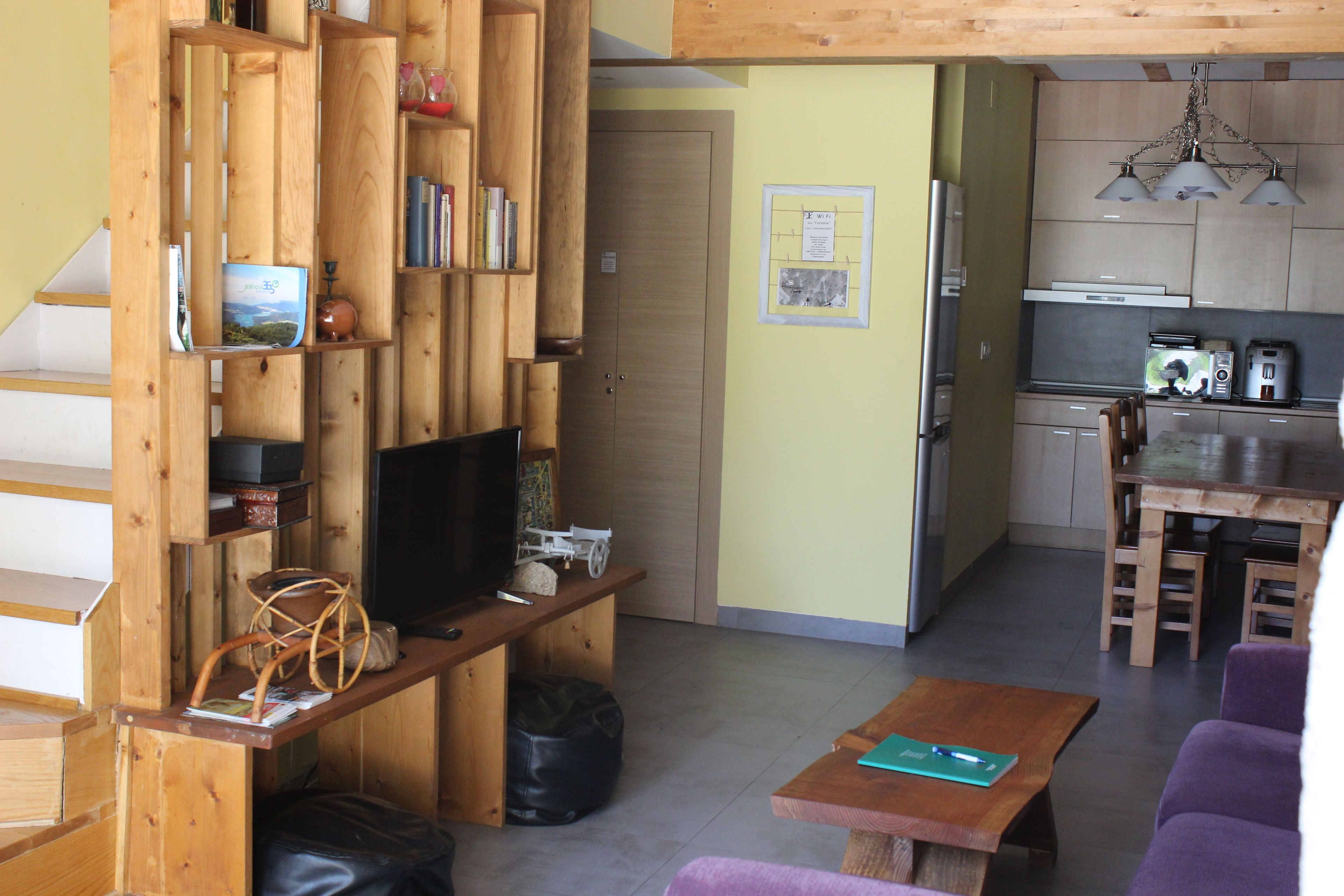 A compact living space with a wooden bookshelf, a television, a dining table, and a kitchen area.