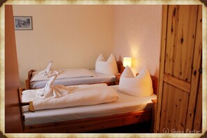 A room with two wooden beds, each with white linens and pillows, a nightstand with a lamp, and a wooden wardrobe. - Hotel Pränzkow (Zwickau)