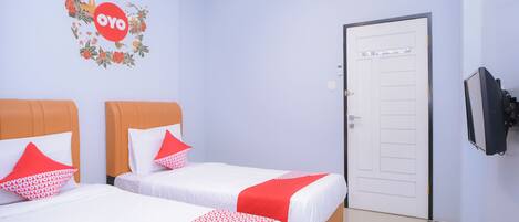 A hotel room with two beds, each with white bedding and red accents, a floral wall decal, and a television on the wall.