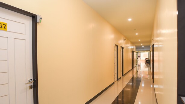 A long, well-lit hallway with a white door labeled "G7" on the left, leading to a room. The walls are beige, and the floor is tiled with a black and white pattern. - Collection O Banda Aceh near Masjid Raya Baiturrahman formerly Hotel Mulana (Banda Aceh)