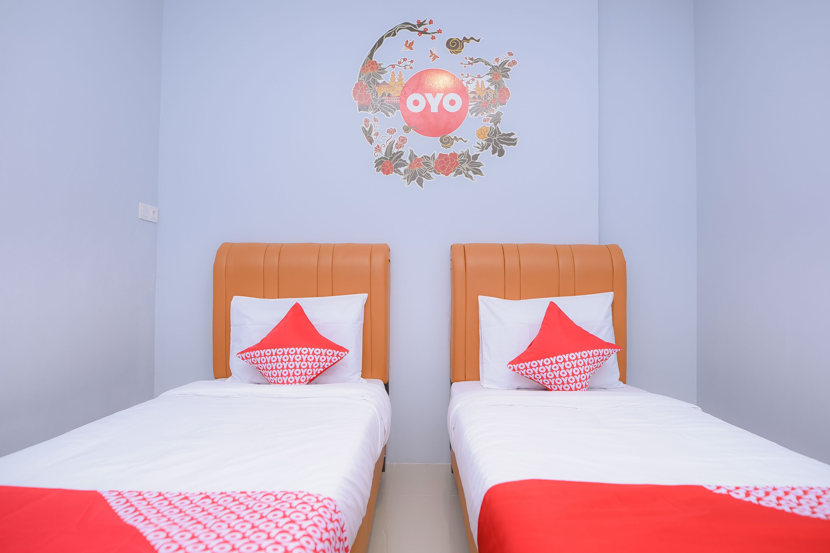 Ein Hotelzimmer mit zwei Betten, jeweils mit weißer Bettdecke und roten Kissen, sowie einer Wandsticker mit dem Schriftzug "OYO".