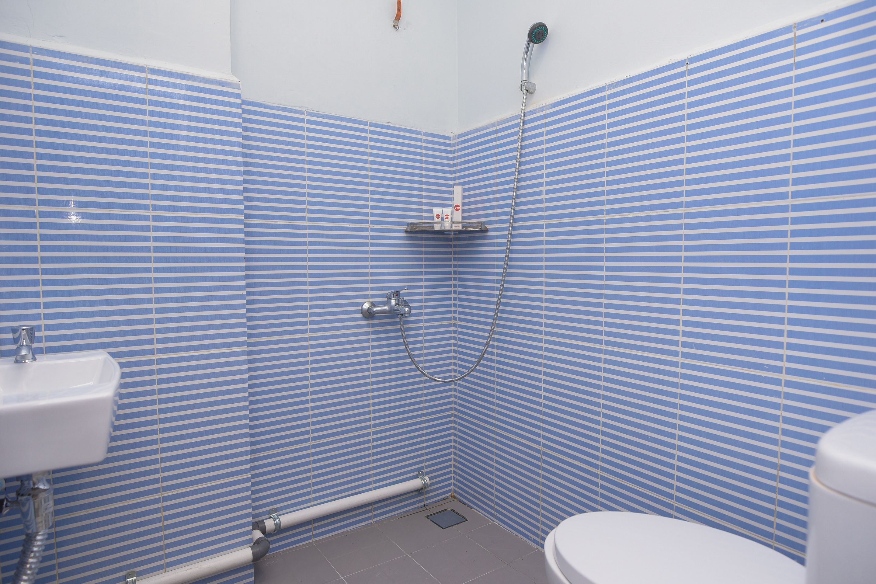 Une salle de bain avec des carreaux bleus à rayures, un lavabo blanc, une douche et des toilettes.