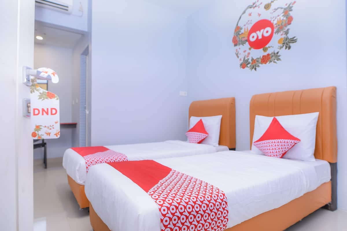 Une chambre d’hôtel avec deux lits, un bureau avec une chaise et un climatiseur fixé au mur.