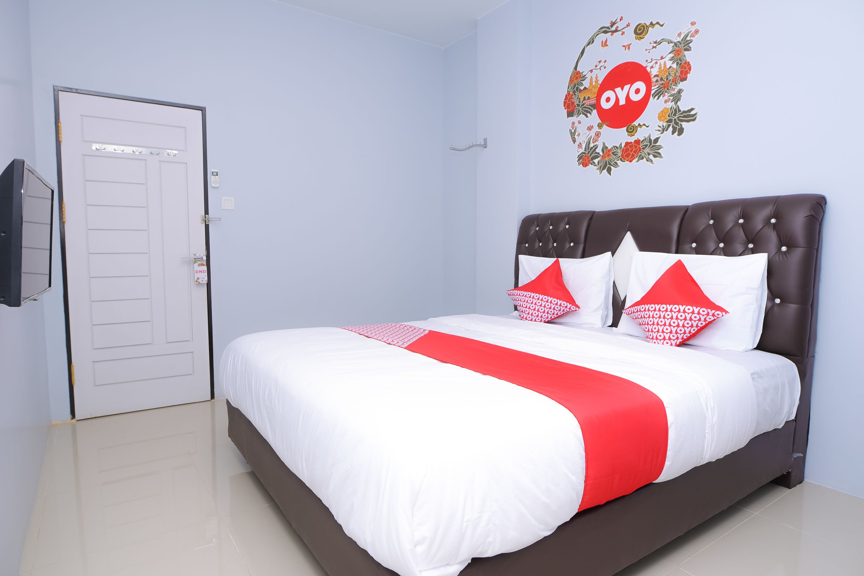 Una cama bien hecha con una colcha rojo y blanco, un cabecero oscuro y dos almohadas rojas con diseños blancos.