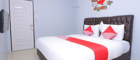 A neatly made bed with a red and white bedspread, a dark headboard, and two red pillows with white patterns.