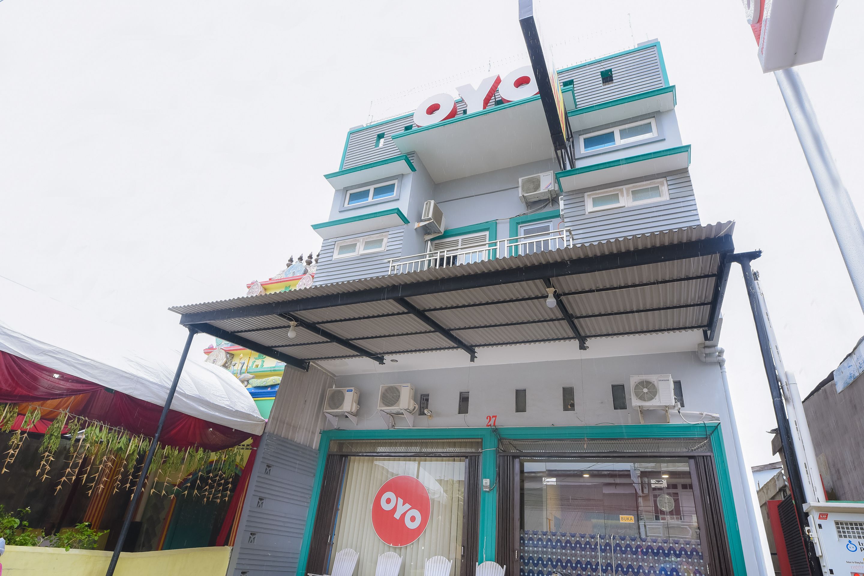 Un edificio con un llamativo letrero 'OYO', unidades de aire acondicionado y un acceso cubierto.