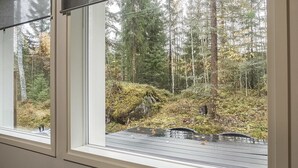 A window with a view of a forested area with trees and a wooden deck.