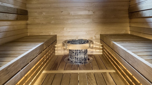 A sauna room with wooden benches, a central heating unit, and a window providing natural light.