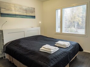 A bedroom with a bed, a window with blinds, a painting on the wall, and a lamp.