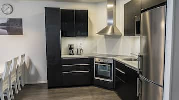 A modern kitchen with black cabinetry, stainless steel appliances, and a wooden floor.