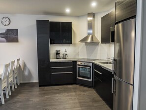 Une cuisine moderne avec des meubles de couleur noire, des appareils électroménagers en acier inoxydable et un plancher en bois.