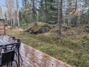 Eine Holzterrasse mit Tisch und Stühlen, umgeben von bewaldetem Gelände mit Steinen und Bäumen.