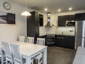 A modern kitchen with dark cabinetry, stainless steel appliances, and a white dining table with chairs.