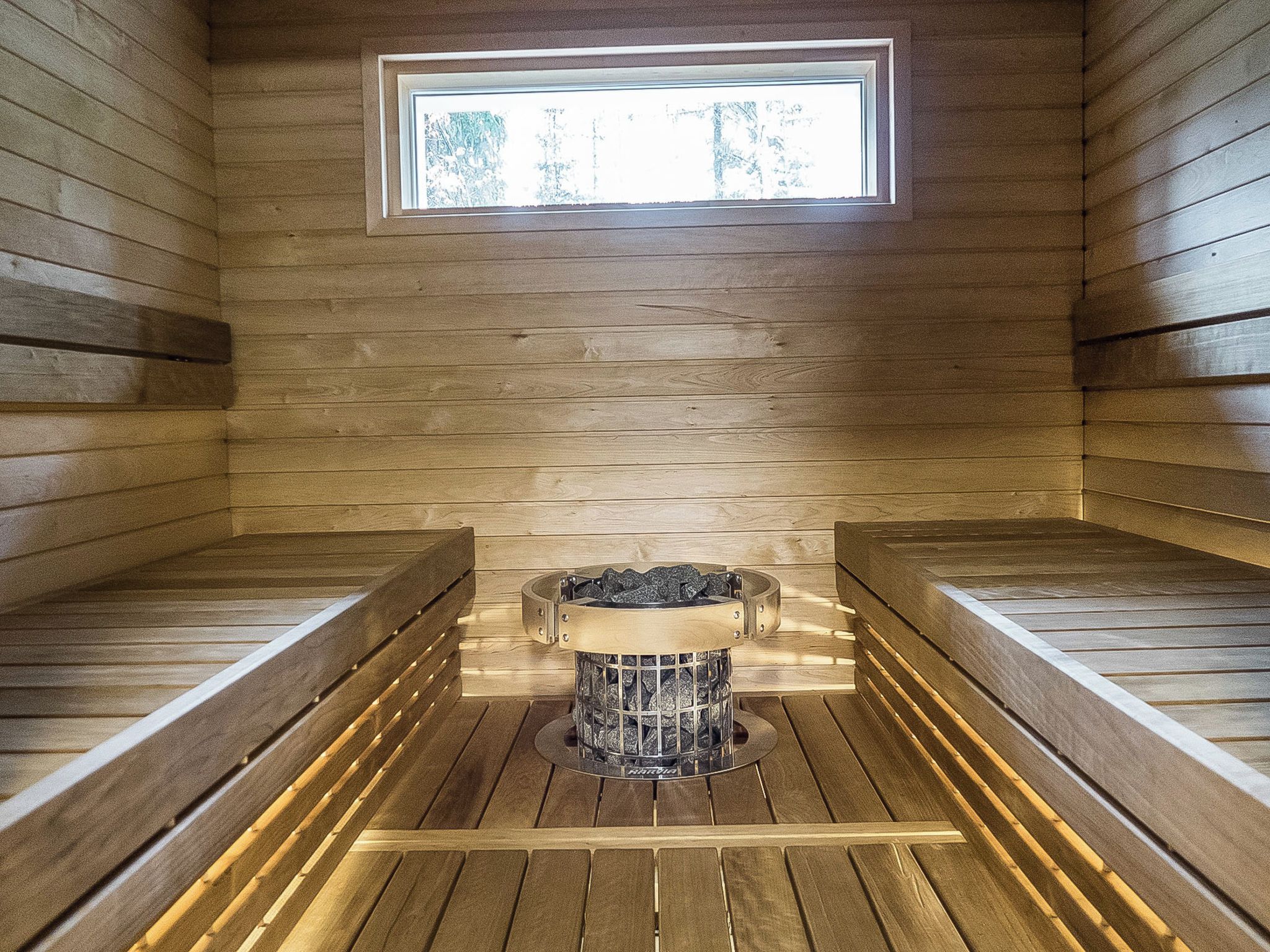 Een sauna met houten banken, een verwarmingsunit en een raam.