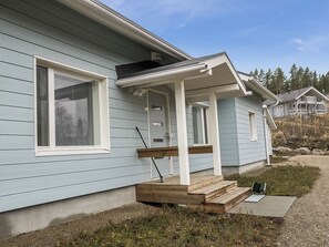 Une maison bleu clair avec un porche, une fenêtre avec des stores et une petite terrasse en bois.