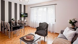 A modern living room with a dining area, a television, and a large window with sheer curtains.
