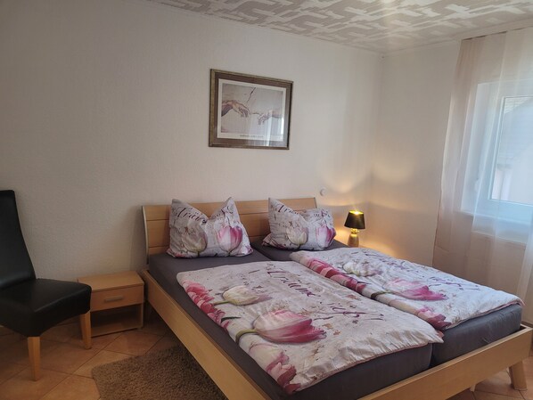 Un dormitorio con cama, dos almohadas, mesita de noche, lámpara y un cuadro en la pared.