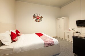 Habitación de hotel con cama, paredes blancas, televisor, armario y pequeño escritorio con silla.