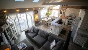Un espacio habitable amplio con un sofá gris, una mesa de comedor y una cocina con armarios blancos y una isla central.