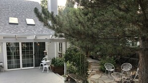 Un patio cubierto con cubierta de madera, muebles de exterior blancos y plantas en macetas.