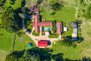 An aerial view of a property with a large red-roofed building, a swimming pool, and a circular driveway.
