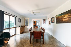 Un vaste espace dédié à la salle à manger, avec une longue table et des chaises, un ventilateur de plafond et des œuvres d’art accrochées aux murs.
