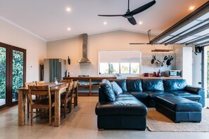 Un espacio habitable moderno con comedor, un sofá de cuero negro y una cocina con un ventanal grande.