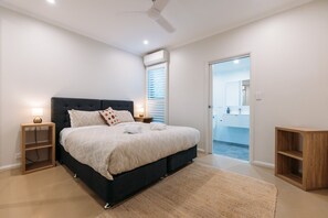 A bedroom with a bed, bedside tables, a ceiling fan, and a view to the bathroom.