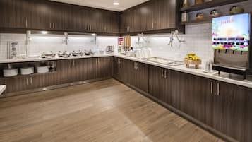 Een moderne keuken met donkerhouten kastjes, witte aanrechtbladen en een ingebouwde sapdispenser.