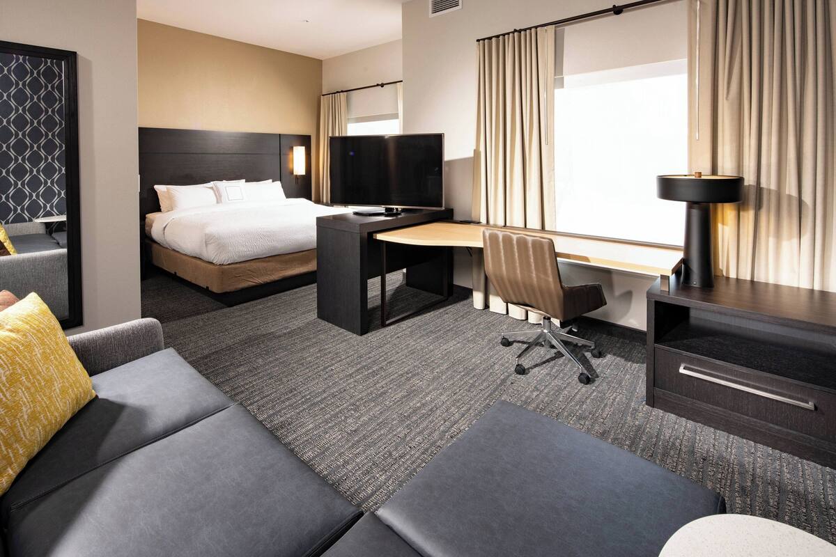 Ein Hotelzimmer mit Bett, Schreibtisch, Sessel, Sofa und Fernseher.