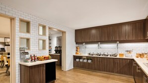 Eine moderne Küche mit Holzschränken, weiß gefliestem Fliesenspiegel und einer zentralen Kochinsel mit verschiedenen Küchenutensilien.