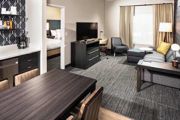 Una habitación de hotel con cama, televisor, escritorio, sofá y mesa de comedor.