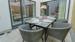 A dining area with a table set for four, surrounded by wicker chairs, and a vase with flowers on the table. - The Larry Mullen Suite - hiphipstay (Dublin)