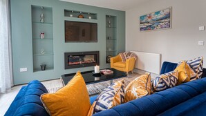 A modern living room with a blue sofa, a yellow armchair, and a fireplace. There are shelves with decorative items and a painting on the wall. - The Larry Mullen Suite - hiphipstay (Dublin)