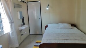Een slaapkamer met een bed, nachtkastje, raam met gordijnen, een wandairconditioner, een deur en een klein vloerkleed.