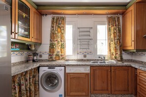 A compact kitchen with wooden cabinets, a built-in washing machine, and a window with curtains. - Stunning apartment on the Golden Mile (Marbella)