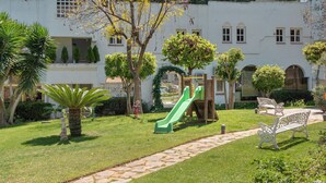 A courtyard with a green slide, a stone pathway, and a white bench. - Stunning apartment on the Golden Mile (Marbella)