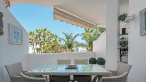A patio with a glass table and wicker chairs, surrounded by white walls and a view of palm trees. - Stunning apartment on the Golden Mile (Marbella)
