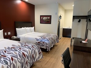 A hotel room with two beds, a desk, a chair, a mirror, a picture on the wall, and a small kitchenette. - Red Roof Inn Houston - Willowbrook (Houston)
