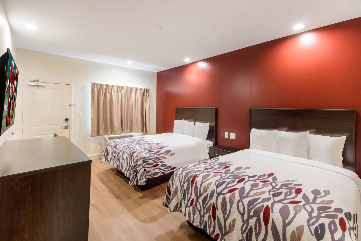 A hotel room with two beds, a desk, and a TV.