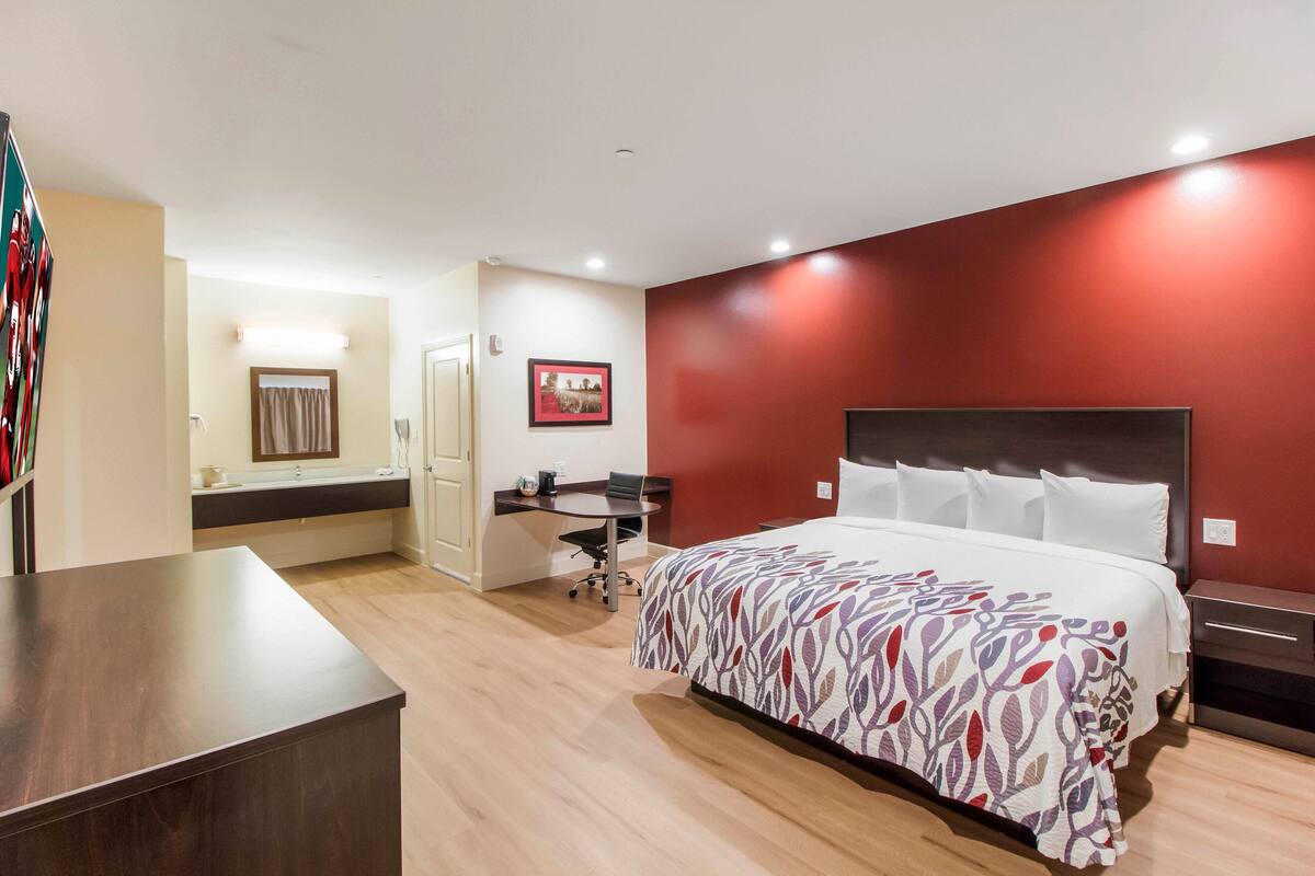 A hotel room with a bed, desk, and a bathroom visible through an open door.