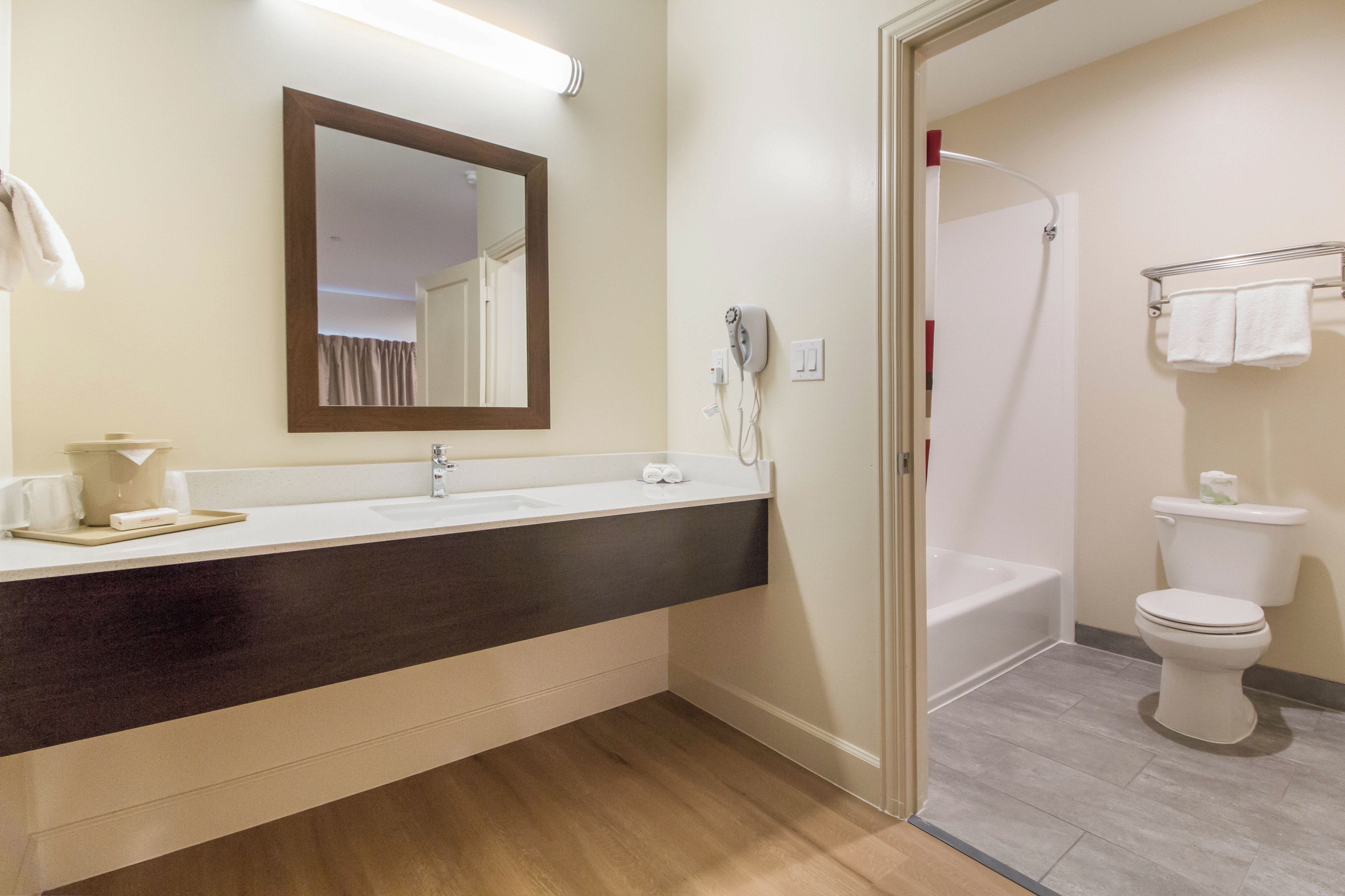 Un baño moderno con una encimera oscura, un espejo, un secador de pelo, una ducha y un inodoro.