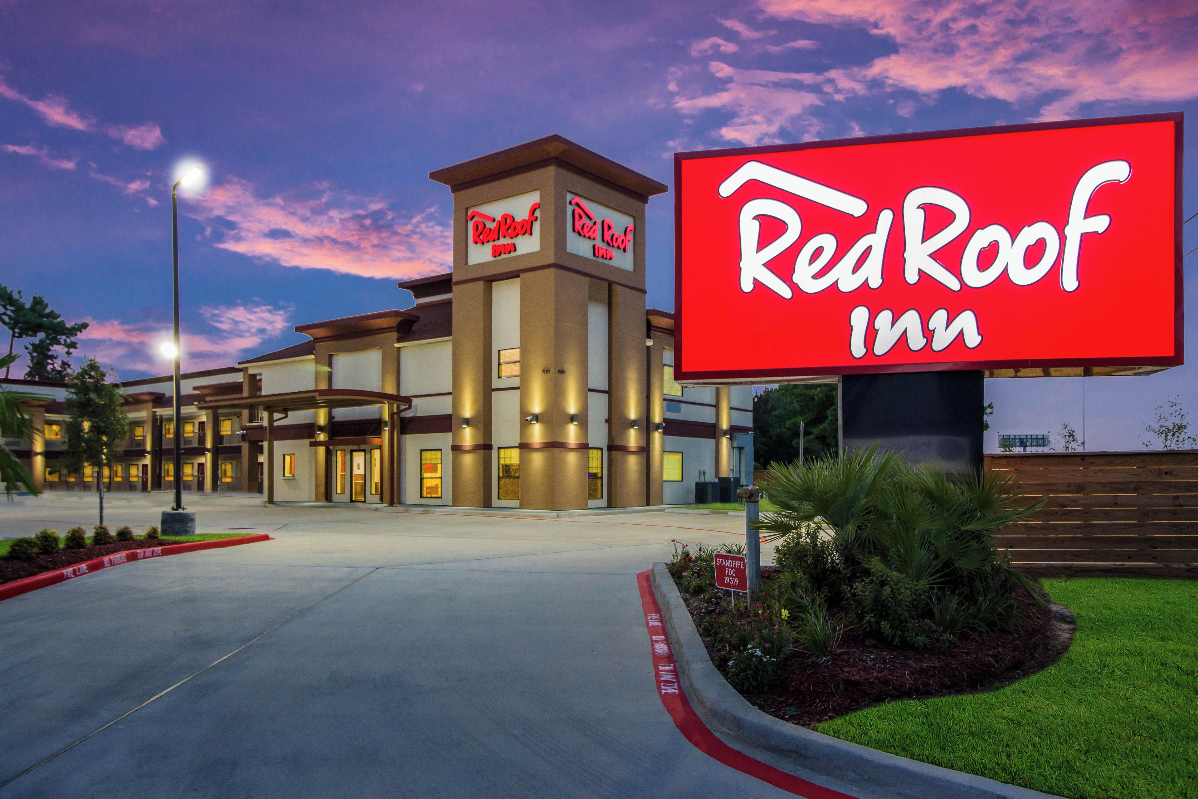 Un Red Roof Inn con señalización llamativa, entrada central y un área ajardinada con plantas.