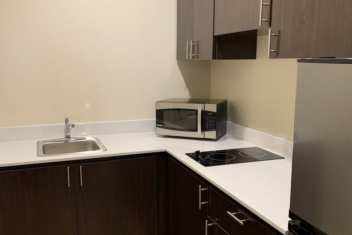 A kitchen with dark cabinets, a microwave, a sink, and a refrigerator.