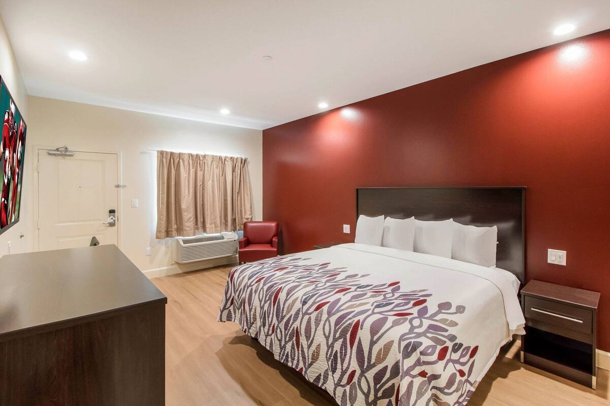 A hotel room with a bed, a desk, a chair, a window with curtains, and a wall unit.
