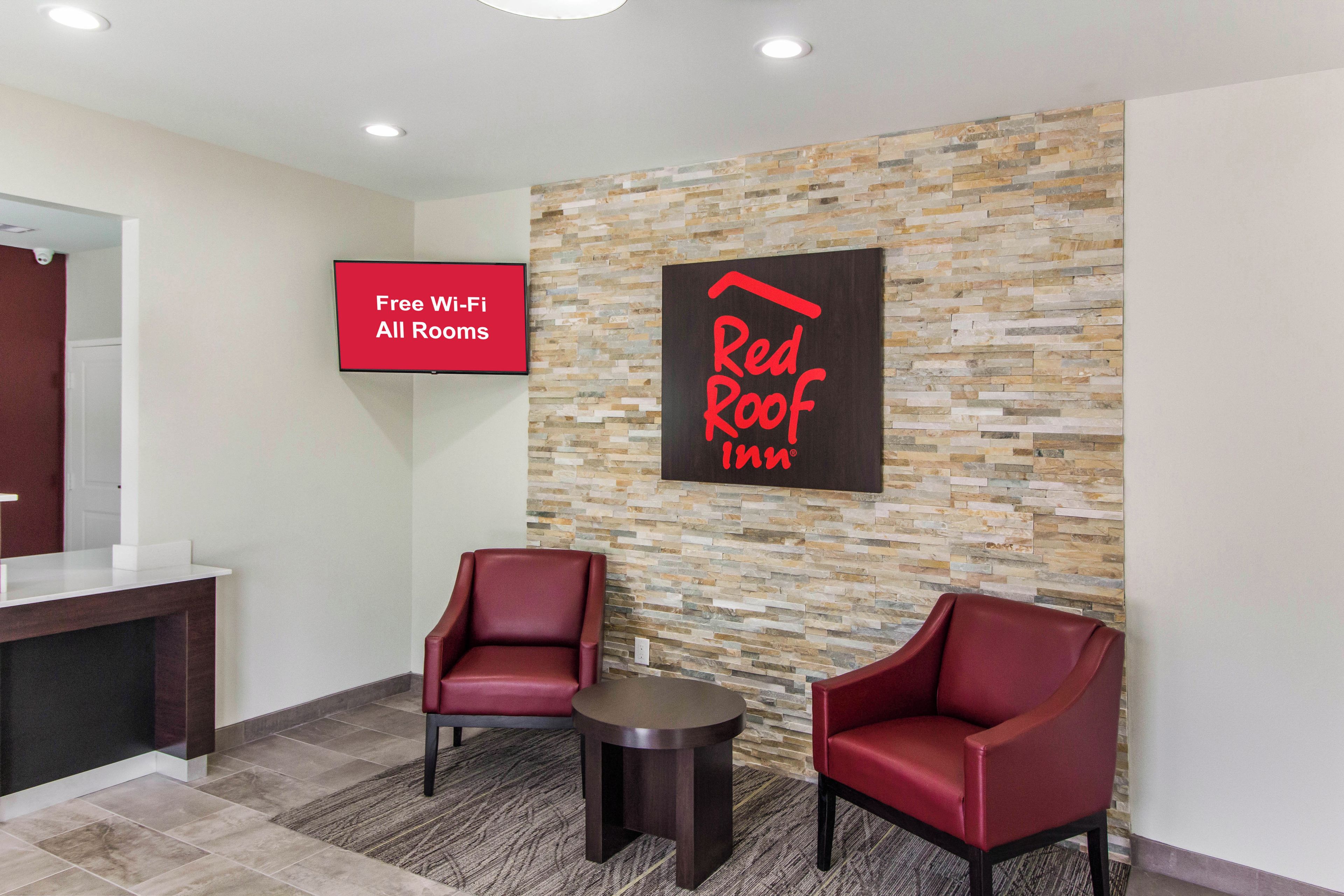 Eine Red Roof Inn Lobby mit zwei roten Sesseln, einem kleinen Tisch und einem Schild, das kostenloses WLAN in allen Zimmern anzeigt.