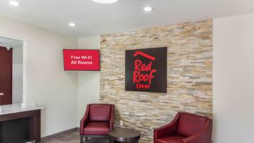 Eine Red Roof Inn Lobby mit zwei roten Sesseln, einem kleinen Tisch und einem Schild, das kostenloses WLAN in allen Zimmern anzeigt.