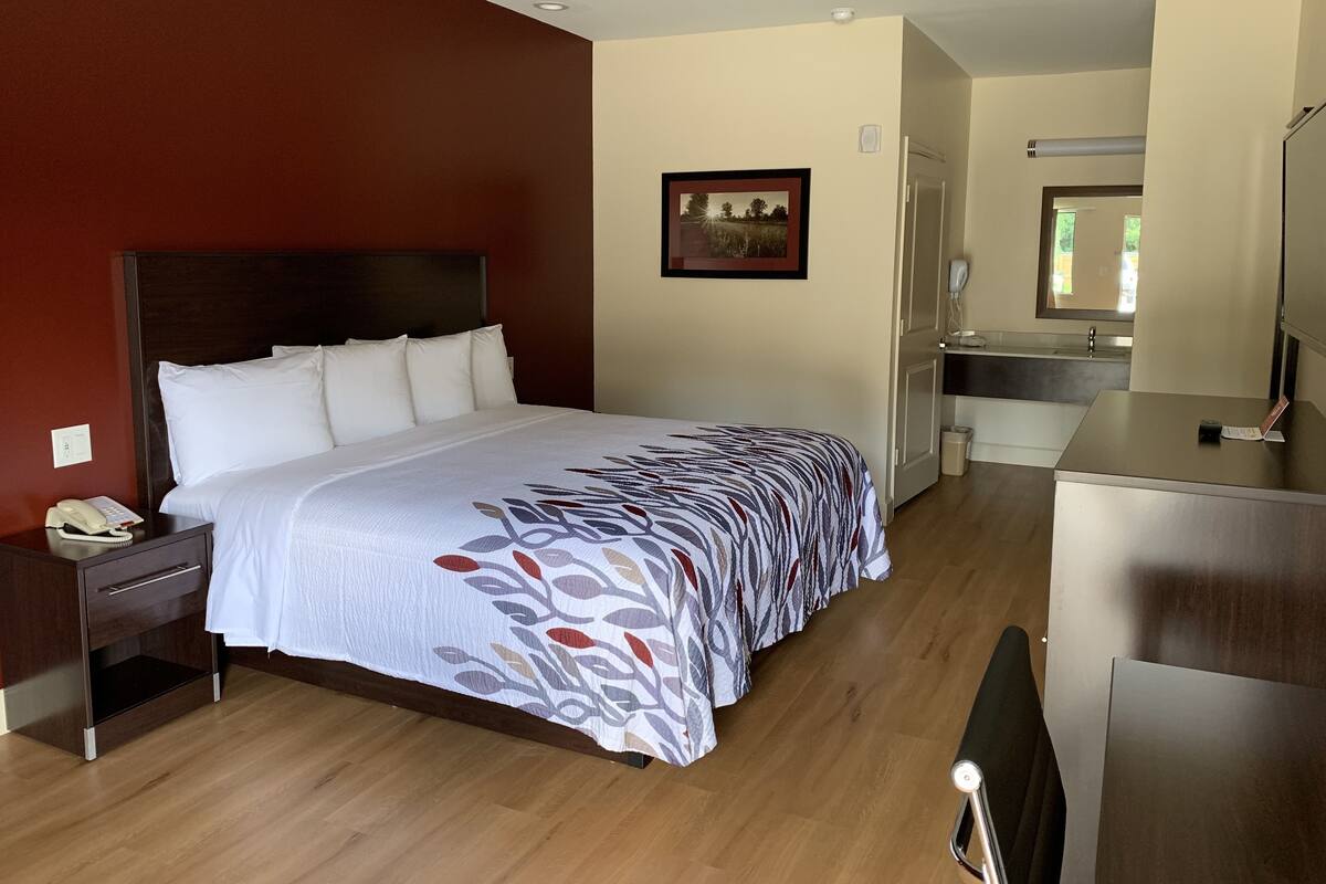 A hotel room with a large bed, a bedside table with a phone, a desk with a chair, and a bathroom visible through an open door.